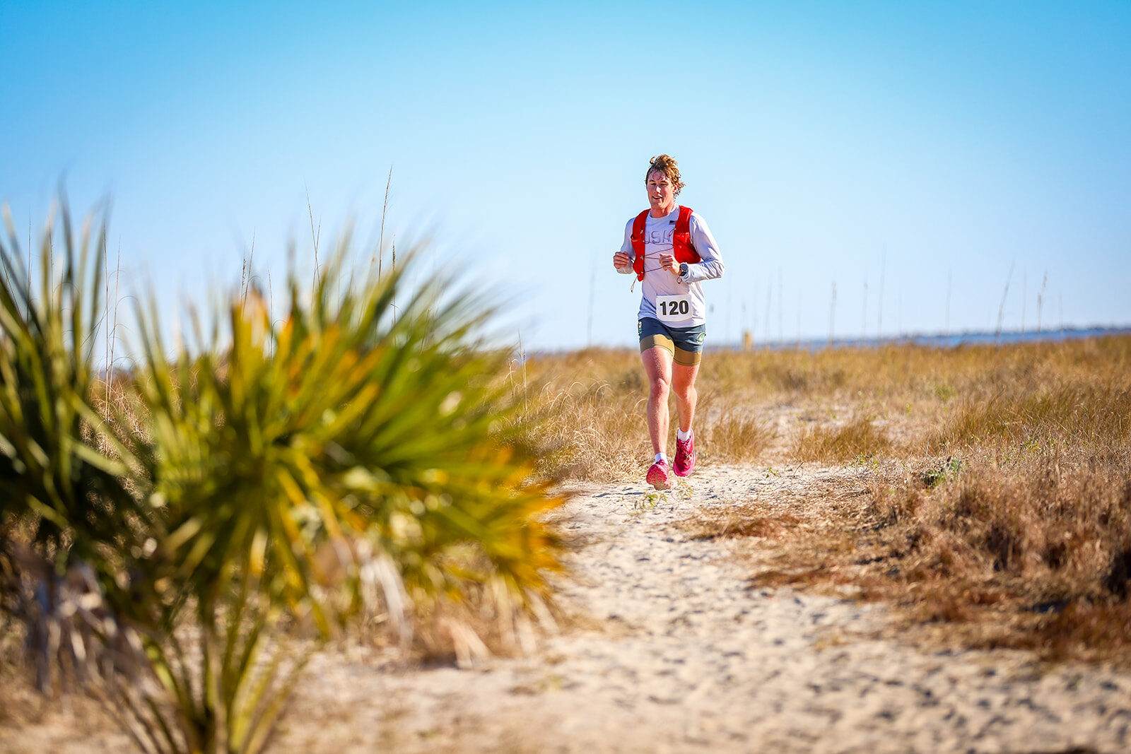 Runner on sandy coastal trail with palmetto foreground